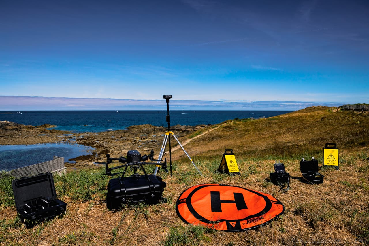 Drone, trépied et balises de sécurité installés sur une lande littorale avant un vol